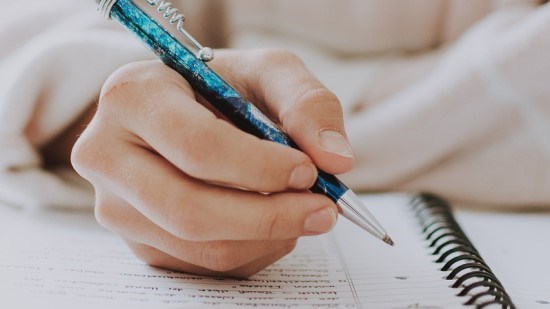 En hand som håller en blå penna och skriver i ett block.