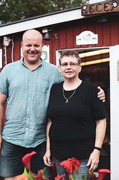 En man och en kvinna står framför ett litet rött hus med vita knutar