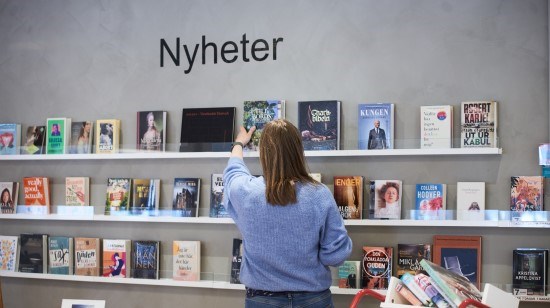 Kvinna som plockar ner en bok från en hylla.