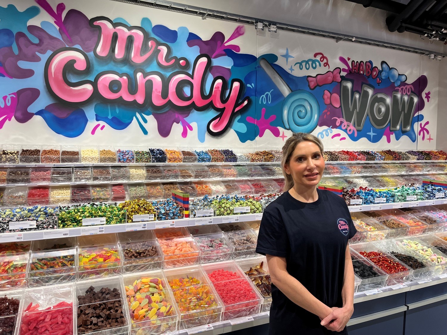 Ägaren Pernilla Abdi står framför lådor med godis och en stor målning på väggen.