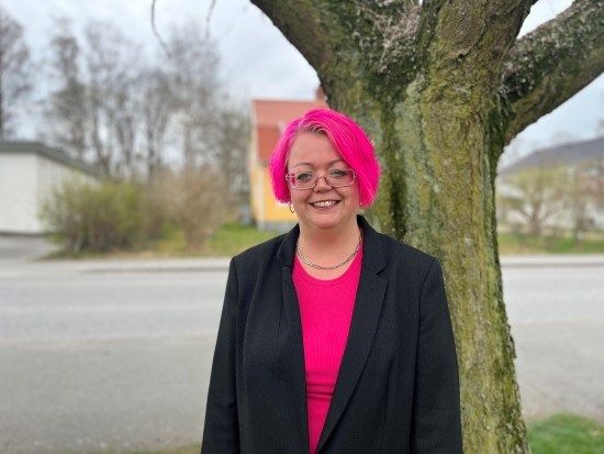 Kvinna med rosa hår står framför ett träd.