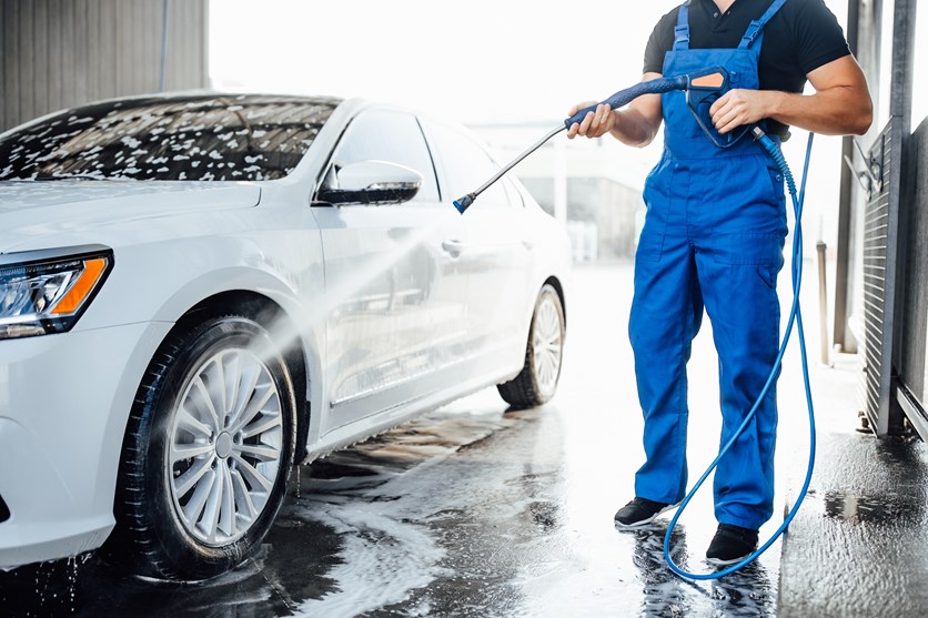 Man i blå byxor tvättar vit bil i tvätthall